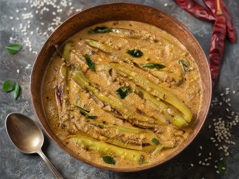 Mirchi ka salan, fried green chillies in a nutty brown gravy with curry leaves, in a copper bowl.