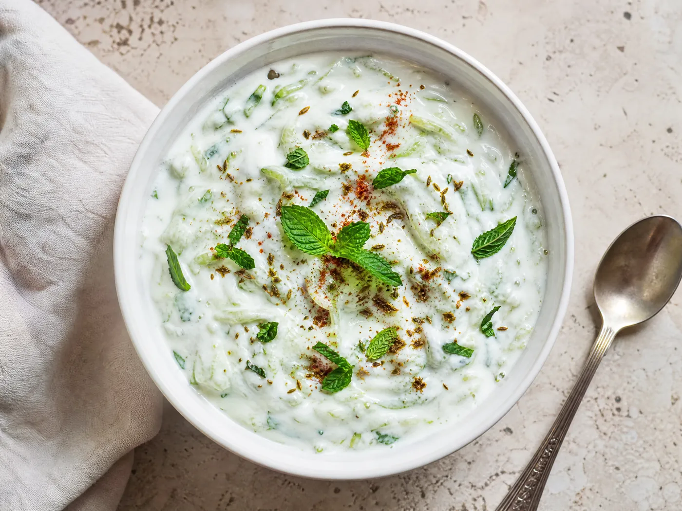A bowl of cucumber raita topped with roasted cumin and mint.