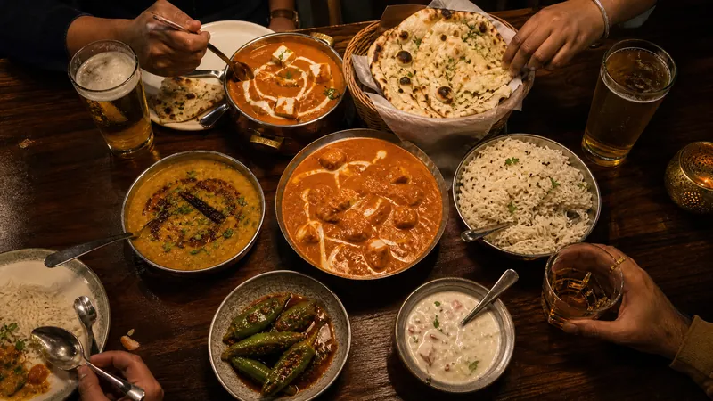 A shared Indian dinner of curries, naan, rice and raita with glasses of lager and whisky.